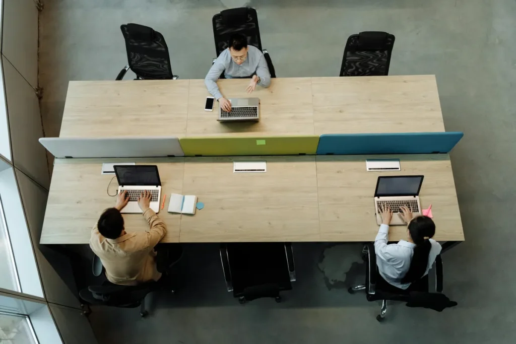 Tiga rekan kerja berkolaborasi di meja kantor menggunakan laptop dalam suasana produktif